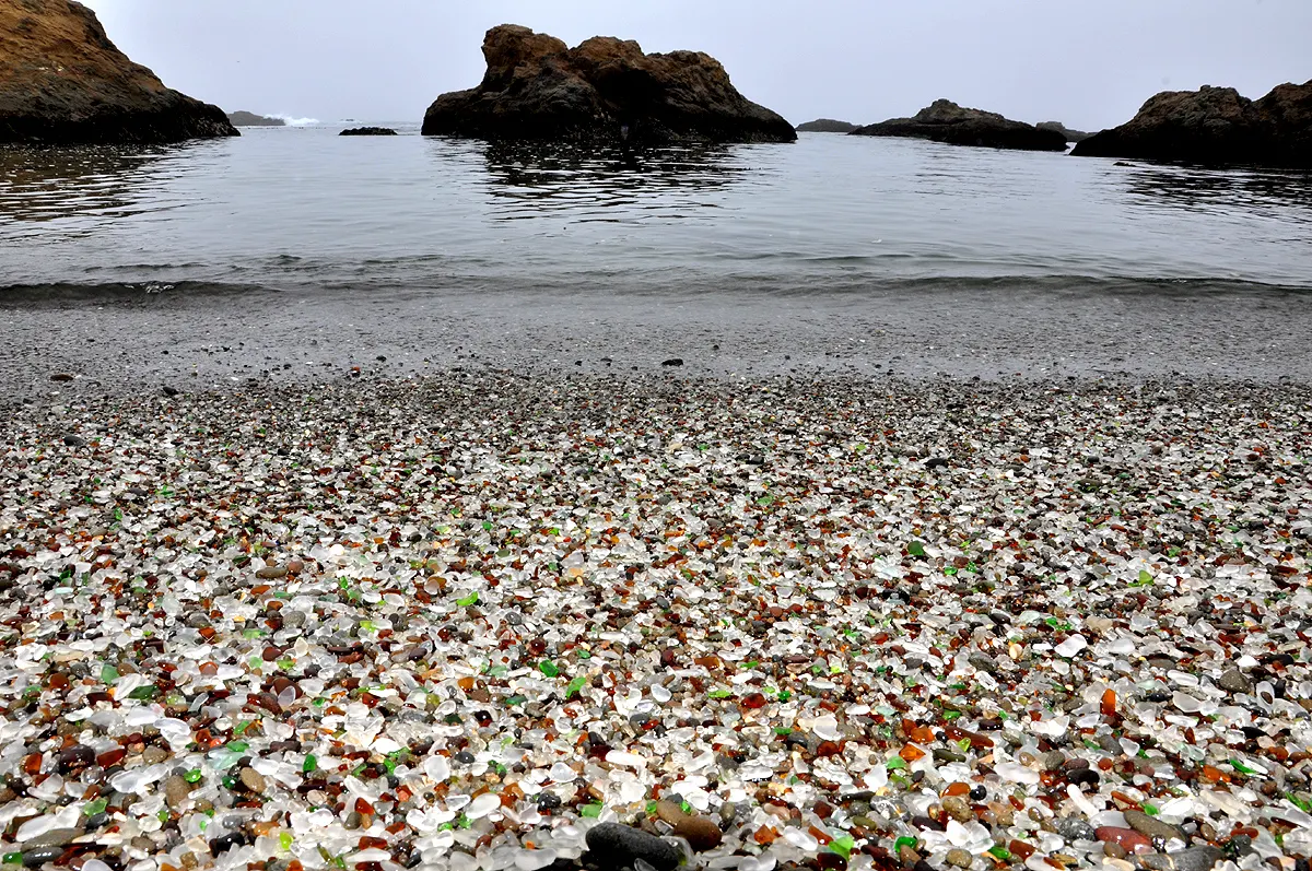 Photo de la plage de verre, avec la mer et des rochers en second plan